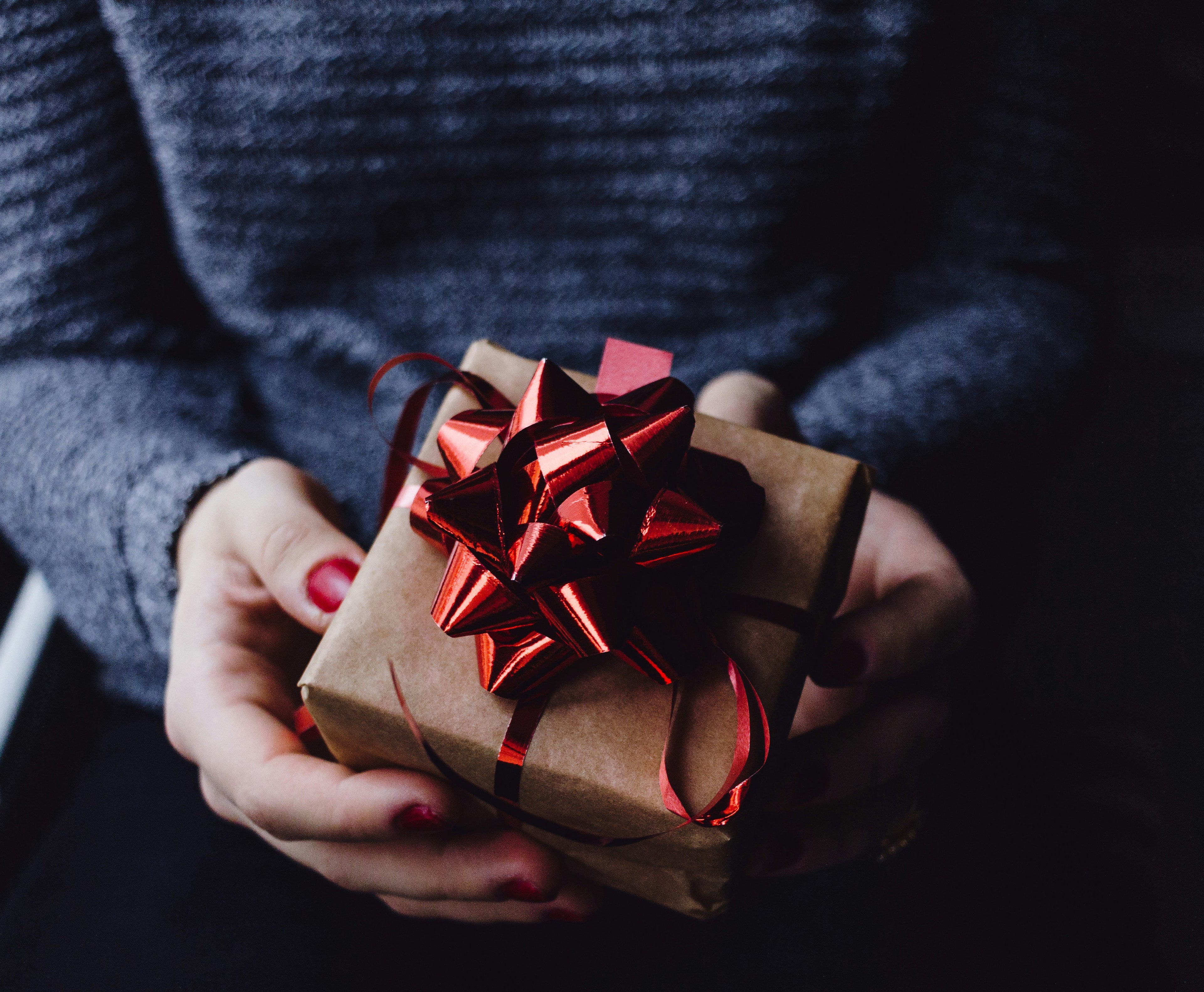 Person holding a small brown gift box with a red ribbon